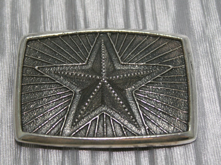 Silver belt buckle featuring a raised five-point star in the center, surrounded by radiating lines in a textured background.
