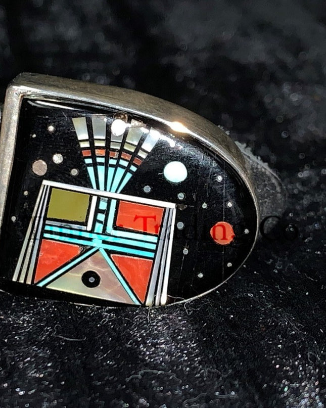 A handcrafted Ranger belt buckle set featuring intricate inlay work. the design incorporates vibrant geometric patterns with black, turquoise, coral, and white inlays, inspired by Southwestern artistry. The bold and colorful patterns are framed by polished silver, enhancing the intricate details. The set is displayed on a black leather belt, resting on a textured dark background.
