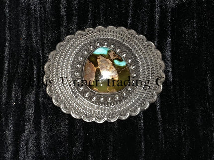A silver belt buckle with a Royston turquoise centerpiece and intricate button details on a black background.