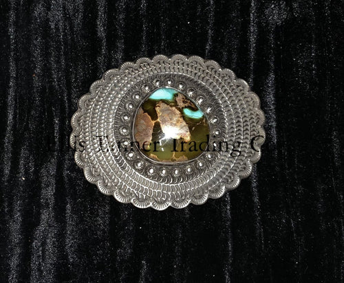 A silver belt buckle with a Royston turquoise centerpiece and intricate button details on a black background.