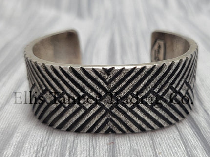 heavy, etched diamond designs front view of bracelet, displayed on top of a silver shiny cloth.