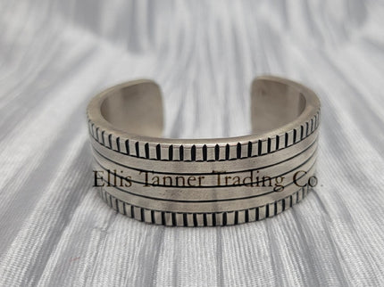 Front View of a heavy silver stamped bracelet, placed on a silver cloth 