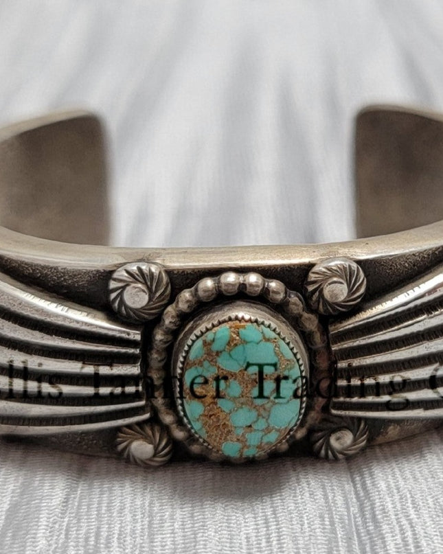 Heavy silver bracelet, with a center Carico Lake Turquoise stone, with an overlay design, on top of a shiny silver sheet 