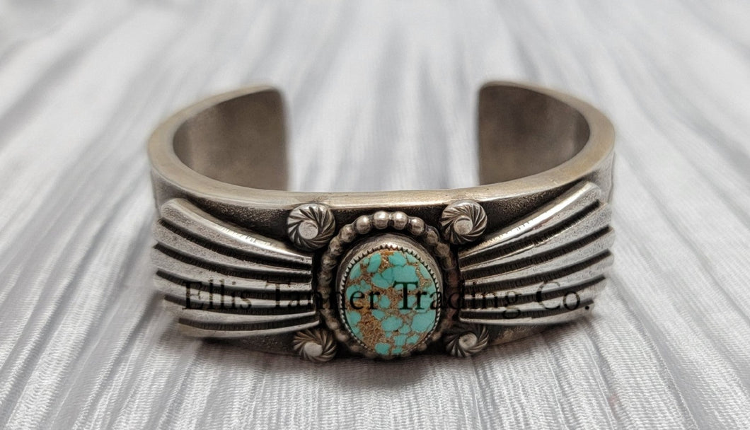 Heavy silver bracelet, with a center Carico Lake Turquoise stone, with an overlay design, on top of a shiny silver sheet 