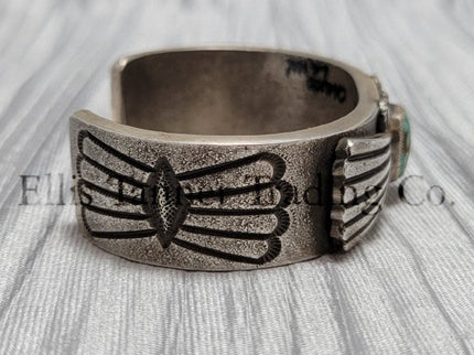 Heavy silver bracelet, with a center Carico Lake Turquoise stone, with an overlay design, on top of a shiny silver sheet 