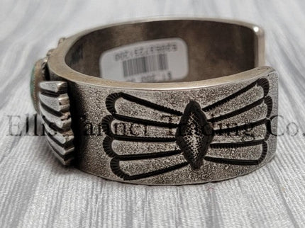 Heavy silver bracelet, with a center Carico Lake Turquoise stone, with an overlay design, on top of a shiny silver sheet side view 