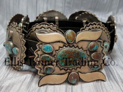 A handcrafted Navajo concho belt with detailed sterling silver conchos, each embedded with mixed turquoise stones of varying shades and natural patterns, attached to a black leather strap. Buckle visible 