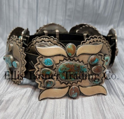 A handcrafted Navajo concho belt with detailed sterling silver conchos, each embedded with mixed turquoise stones of varying shades and natural patterns, attached to a black leather strap. Buckle visible 