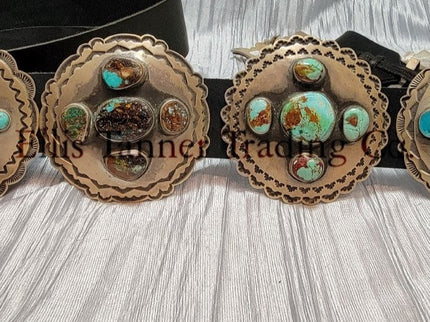 A handcrafted Navajo concho belt with detailed sterling silver conchos, each embedded with mixed turquoise stones of varying shades and natural patterns, attached to a black leather strap.
