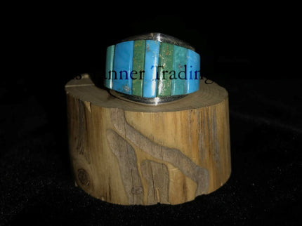 A silver-banded ring with blue and green stone inlays, displayed on a wooden piece, with the brand name 'Inner Trading' visible.