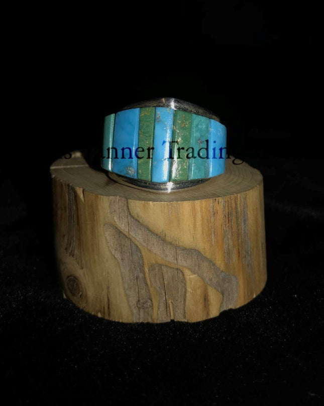 A silver-banded ring with blue and green stone inlays, displayed on a wooden piece, with the brand name 'Inner Trading' visible.