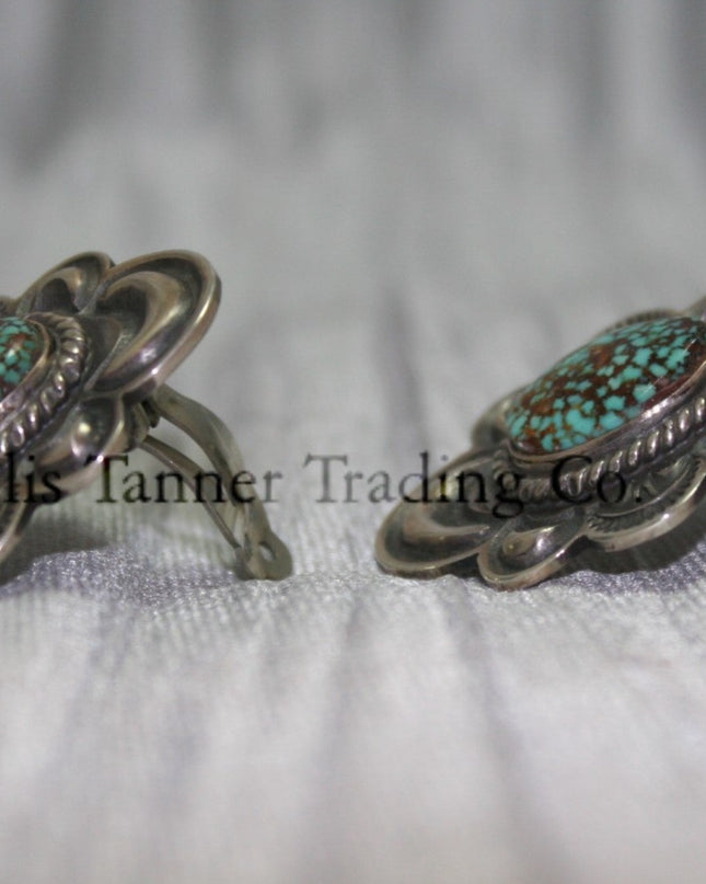Silver stamped clip on earrings, with a center #8 Turquoise surrounded by a silver rope. side view on top of a silver sheet 