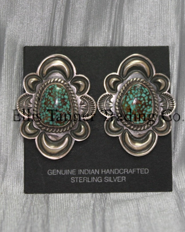 Silver stamped clip on earrings, with a center #8 Turquoise surrounded by a silver rope. displayed on a black card on top of a silver sheet 