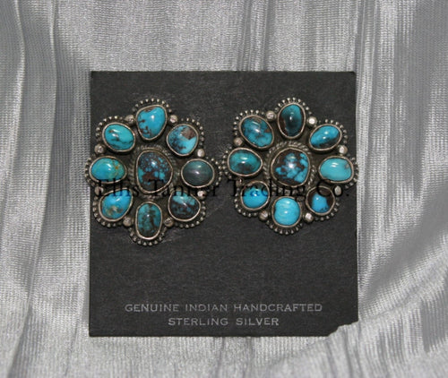 Cluster-style sterling silver clip-on earrings featuring polished turquoise stones with brown matrix patterns, arranged in a floral design with bead accents, displayed on a black card against a silver satin background.