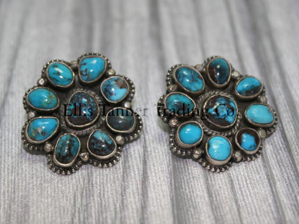 Cluster-style sterling silver clip-on earrings featuring polished turquoise stones with brown matrix patterns, arranged in a floral design with bead accents, displayed on a black card against a silver satin background.