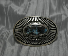 Load image into Gallery viewer, Oval shaped buckle, with a center Black diamond turquoise stone, displayed on top of a shiny silver sheet 
