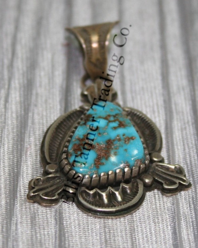Silver Pendant, over lay silver with hand stamped designs. A center Kingman stone surrounded by a silver bezel. placed on top of a shiny cloth 