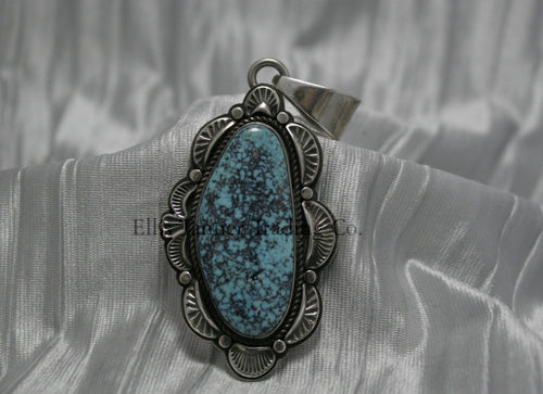 A handcrafted sterling silver pendant with a Morenci Turquoise gemstone. The stone is blue with a black and gray matrix and is set in an ornate silver frame with scalloped and stamped detailing. The pendant features a large bail for easy attachment to a chain.