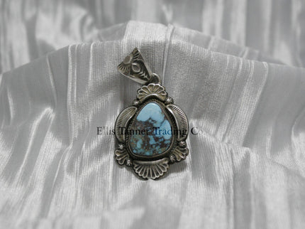 Teardrop-shaped Bisbee turquoise pendant set in sterling silver with intricate engraved details, scalloped accents, and an ornate bail, displayed on a white satin background.
