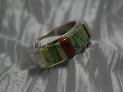 A silver bracelet featuring an intricate cobblestone inlay design with vibrant Carico Lake turquoise and coral stones. The piece is displayed on a soft, textured silver-gray fabric, side profile 