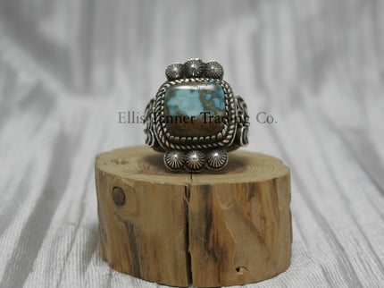 Tommy Jackson Square Royston Turquoise, three stamped buttons on top and bottom of stone, on top of a wooden display.