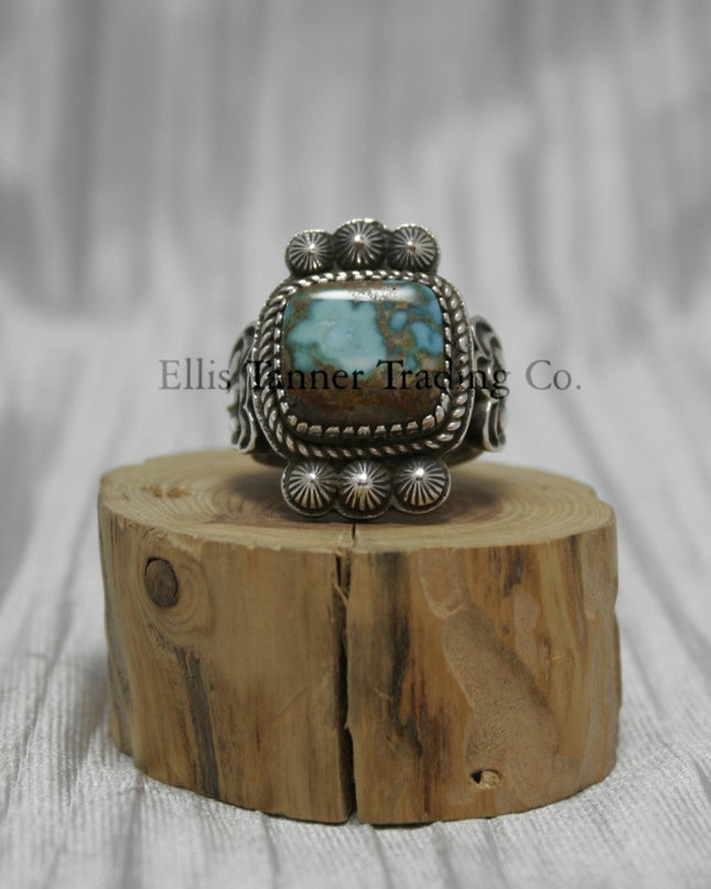 Tommy Jackson Square Royston Turquoise, three stamped buttons on top and bottom of stone, on top of a wooden display.